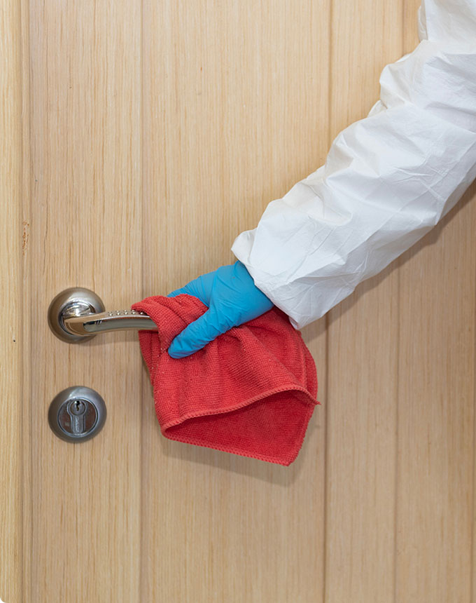 Close-up image of a cleaner disinfecting the doorknobs with red microfiber cloth.