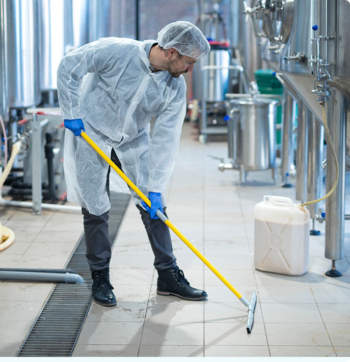 Man in coverall suit and hairnet, cleaning the floor of a warehouse in Denver
