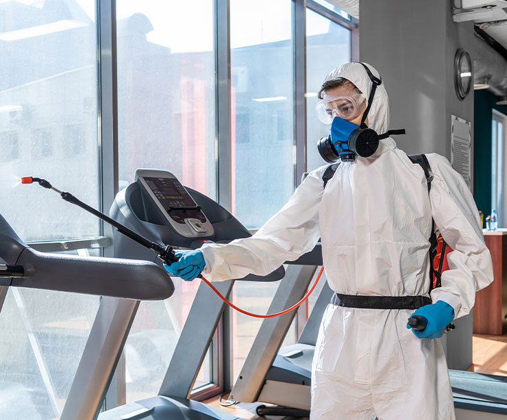 Commercial cleaner in white coveralls wiping the arm of a treadmill at a Denver fitness center.