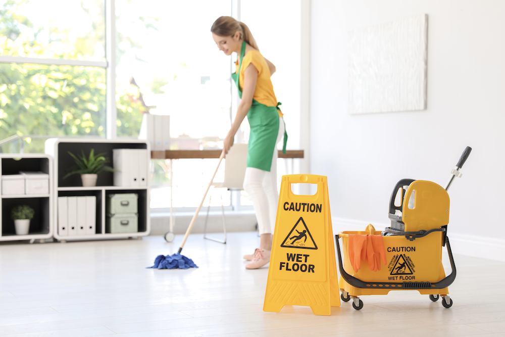Woman specializing in various types of commercial cleaning services, mops office with Wet Floor Sign up