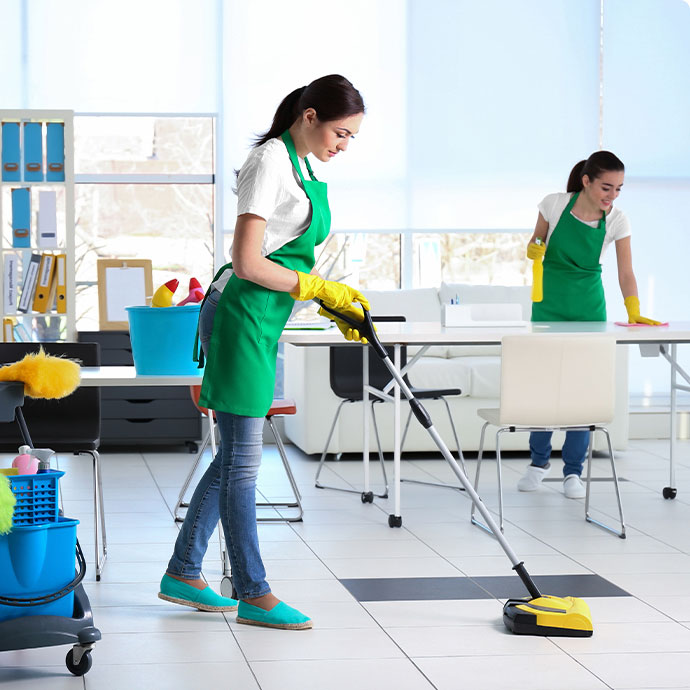Two female cleaners in green aprons providing office cleaning in Dallas.