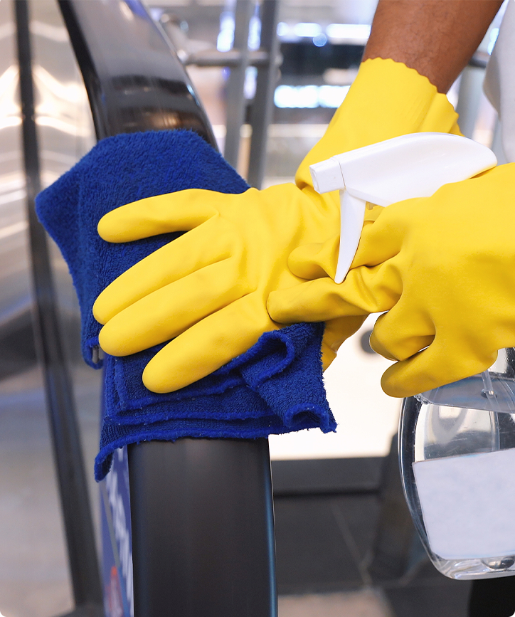 Close up image of cleaner disinfecting handrails at retail store with yellow gloves and microfiber cloth.