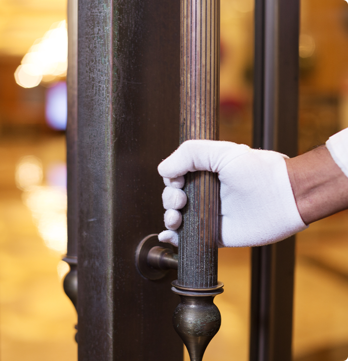Closeup of a professional porter cleaning a door handle with white gloves.