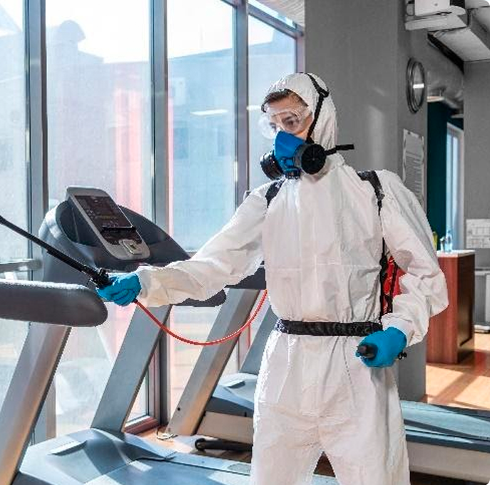 Commercial cleaner in white coveralls wiping the arm of a treadmill at a Dallas fitness center.