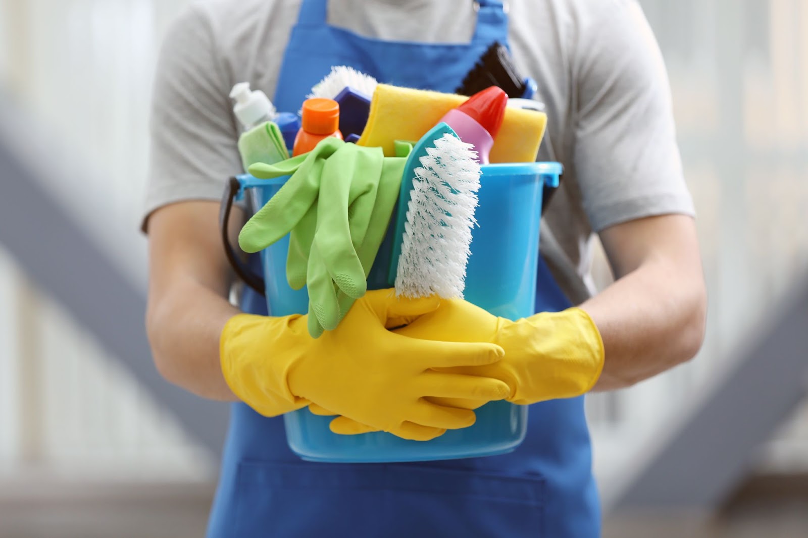 Commercial cleaner holding a bucket of cleaning supplies while wearing yellow rubber gloves.